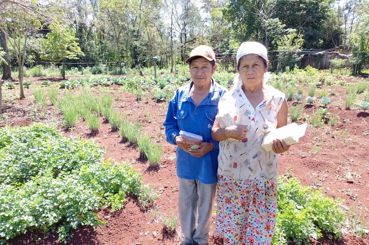 João Cunumi e Catalina Noceda seguram sementes de feijão em meio à plantação de hortaliças na Tekoha Oco’y / Foto: Erison de Jesus Moreira